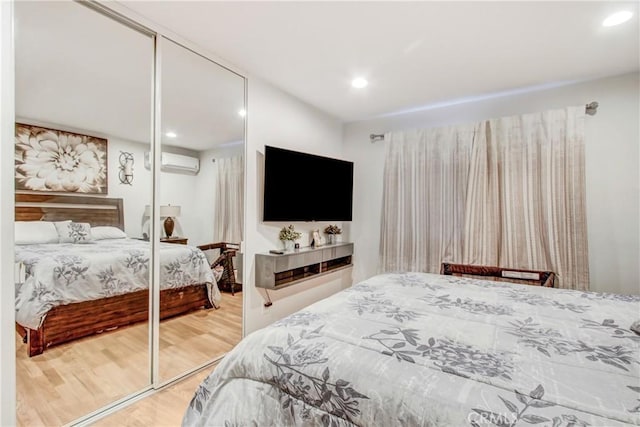 bedroom featuring a wall unit AC, a closet, wood finished floors, and recessed lighting