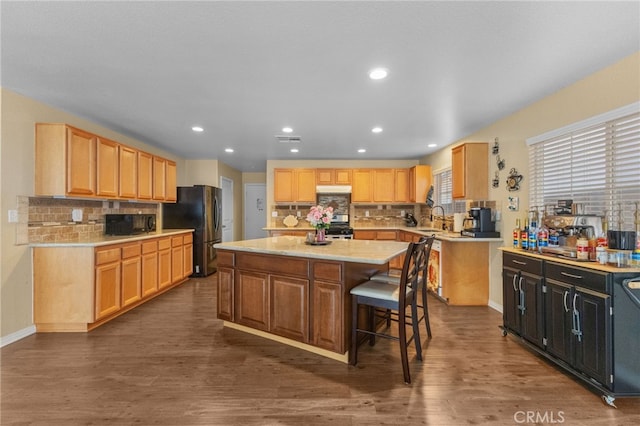 kitchen with a center island, freestanding refrigerator, a sink, black microwave, and a kitchen breakfast bar