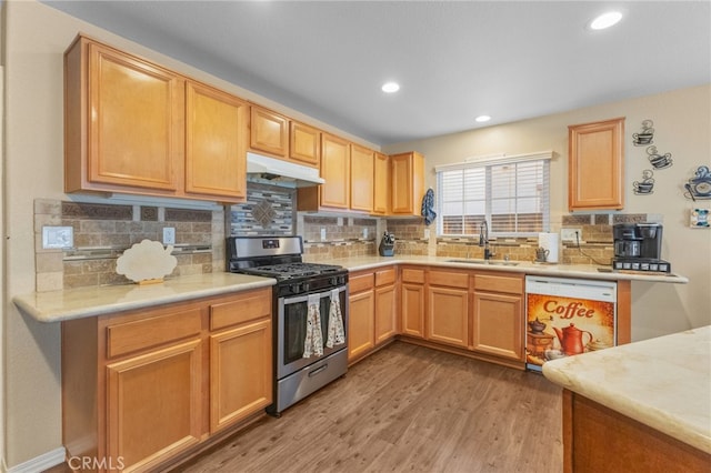 kitchen with stainless steel gas range, white dishwasher, light countertops, under cabinet range hood, and a sink