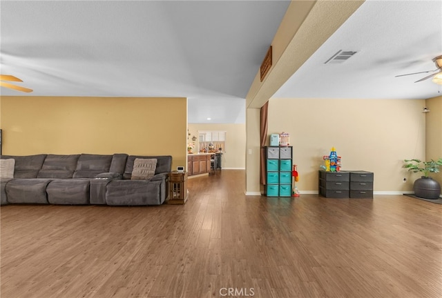 living area with ceiling fan, wood finished floors, visible vents, and baseboards