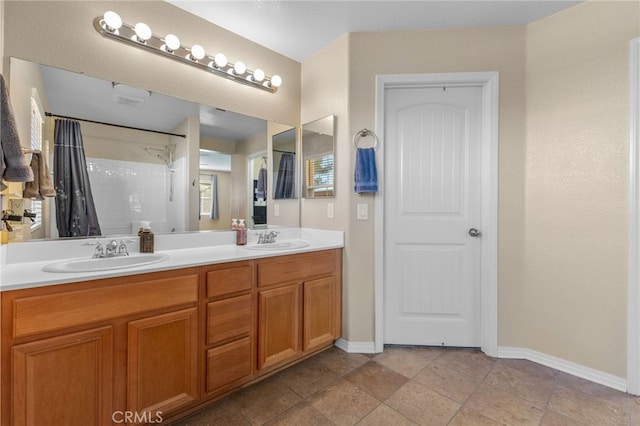 bathroom with double vanity, a shower, a sink, and baseboards