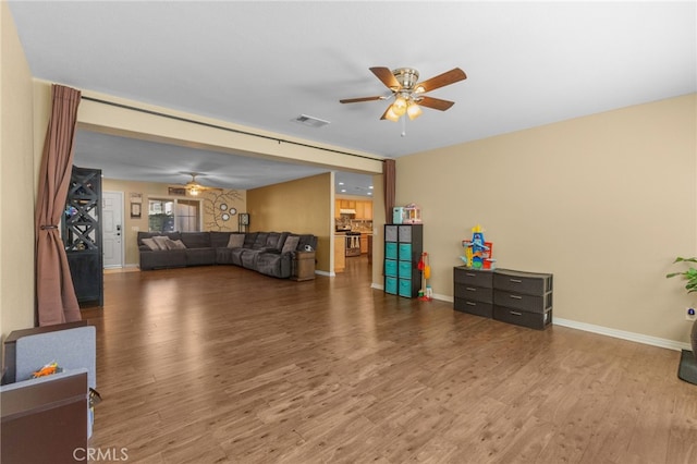 living area with a ceiling fan, visible vents, baseboards, and wood finished floors