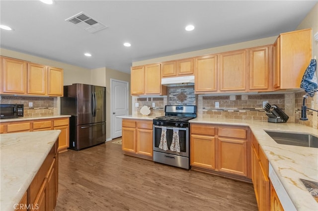 kitchen with black microwave, under cabinet range hood, visible vents, stainless steel gas range, and freestanding refrigerator