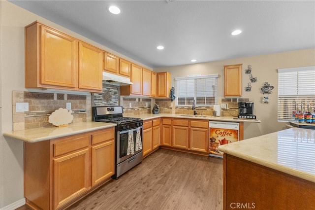 kitchen featuring light countertops, white dishwasher, a sink, under cabinet range hood, and stainless steel gas range oven