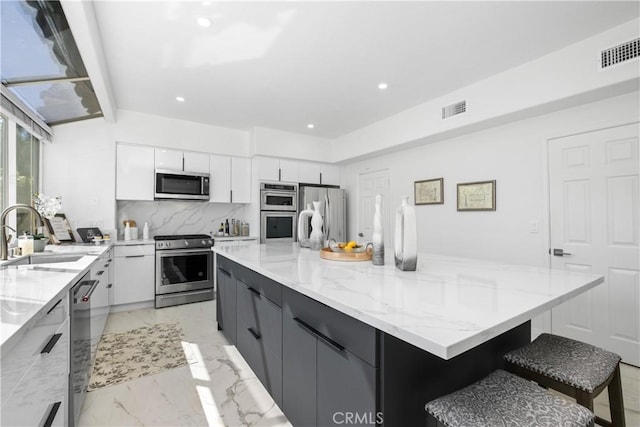 kitchen with a spacious island, a sink, a kitchen breakfast bar, white cabinets, and appliances with stainless steel finishes