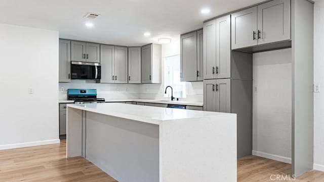 kitchen featuring stainless steel appliances, a sink, visible vents, light countertops, and a center island