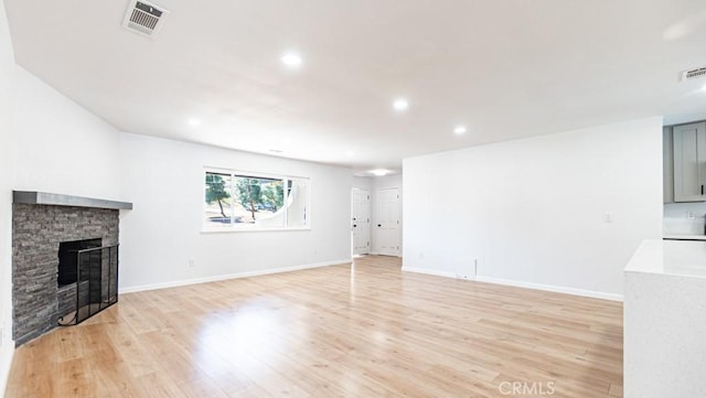 unfurnished living room with light wood-style flooring, visible vents, a stone fireplace, and baseboards