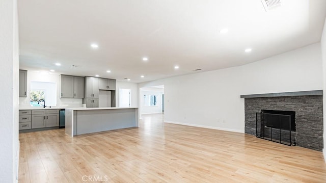 unfurnished living room featuring a stone fireplace, recessed lighting, a sink, visible vents, and light wood finished floors