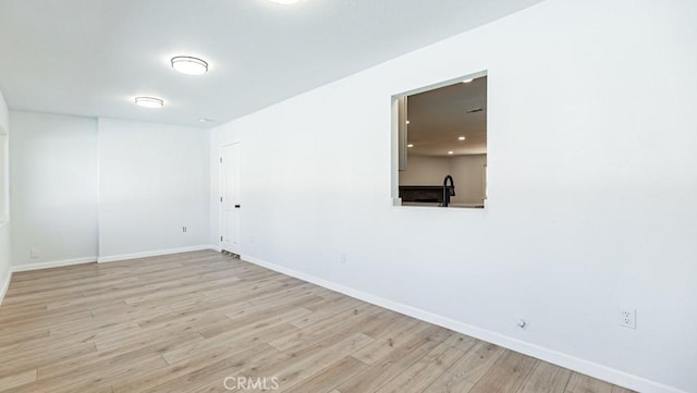 spare room with baseboards, a sink, and light wood finished floors