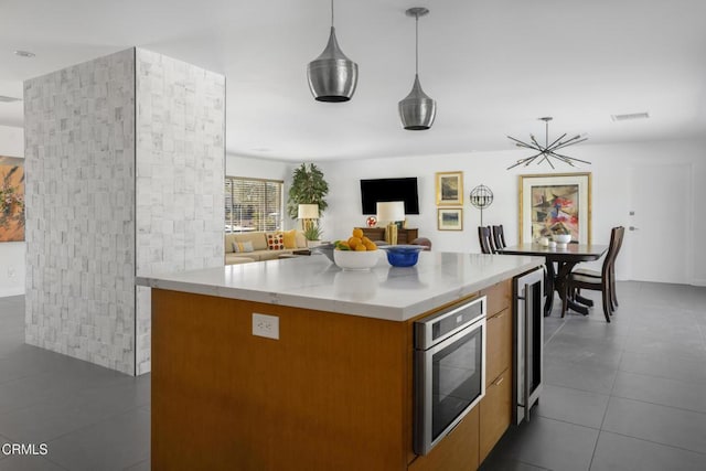 kitchen with pendant lighting, brown cabinets, light countertops, open floor plan, and beverage cooler