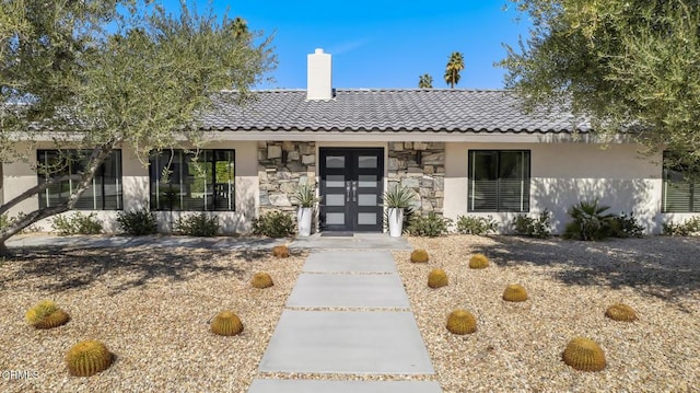 ranch-style home with stone siding, a tile roof, a chimney, and stucco siding