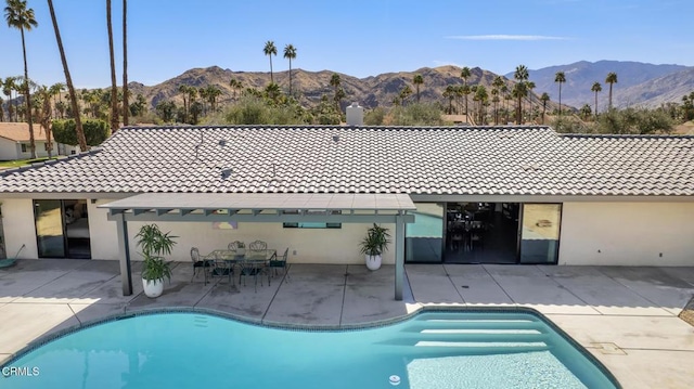 rear view of property with a tile roof, a patio, stucco siding, a mountain view, and an outdoor pool