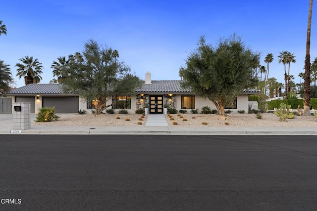 view of front of property featuring a tile roof, a chimney, stucco siding, an attached garage, and driveway