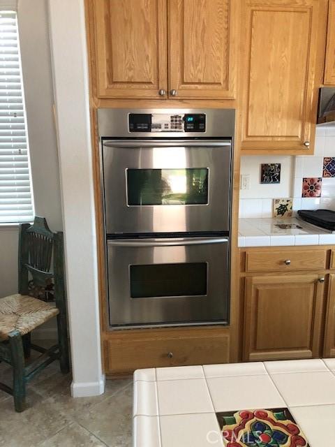 kitchen with baseboards, tile counters, brown cabinets, and stainless steel double oven