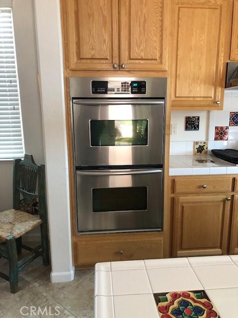 14510 Spyglass Cir, Chowchilla, CA 93610 - kitchen with stainless steel double oven, tile countertops, tile patterned flooring, and baseboards