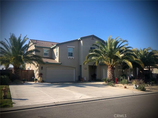 mediterranean / spanish house with a garage, concrete driveway, a tiled roof, fence, and stucco siding