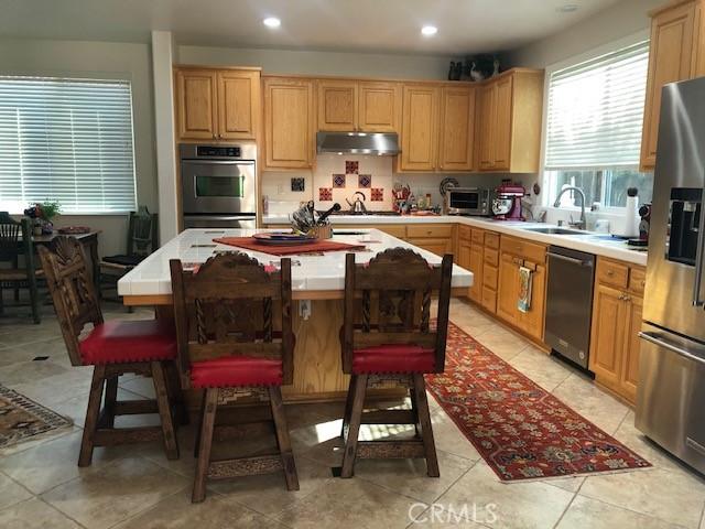 kitchen with light countertops, appliances with stainless steel finishes, a kitchen island, a sink, and under cabinet range hood