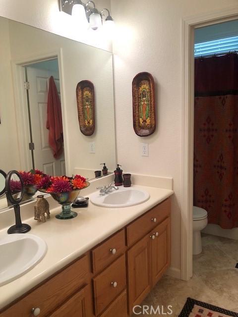 full bath featuring tile patterned floors, a sink, toilet, and double vanity