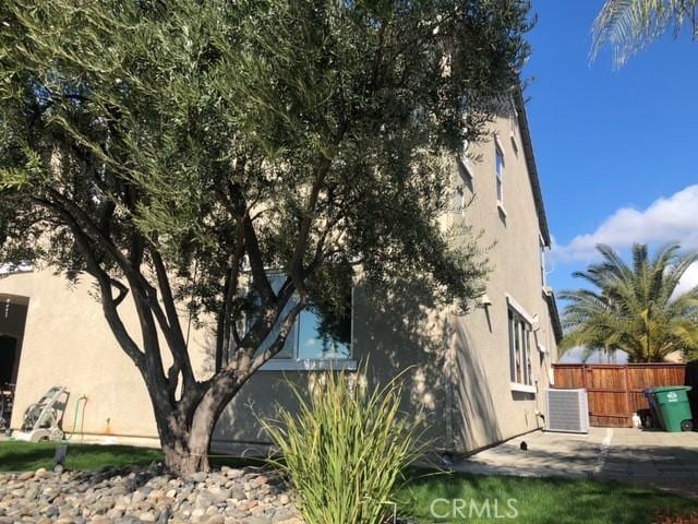 view of side of home featuring cooling unit, a patio area, fence, and stucco siding