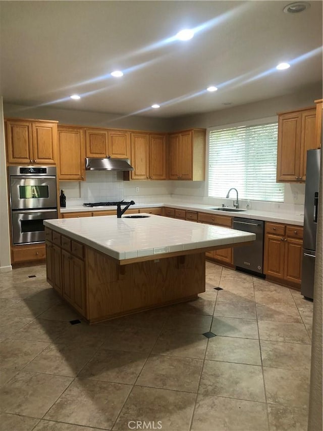 14510 Spyglass Cir, Chowchilla, CA 93610 - kitchen with stainless steel appliances, under cabinet range hood, a sink, tile counters, and an island with sink