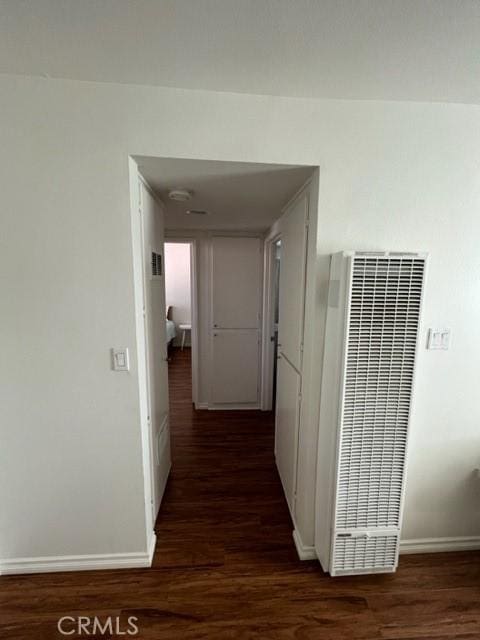 hall featuring baseboards, a heating unit, and dark wood finished floors