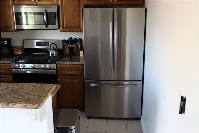 kitchen featuring appliances with stainless steel finishes, dark stone counters, and brown cabinets