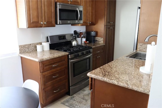 kitchen with stainless steel appliances, brown cabinets, a sink, and light stone countertops