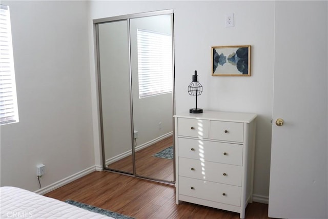 bedroom with dark wood-type flooring, a closet, and baseboards