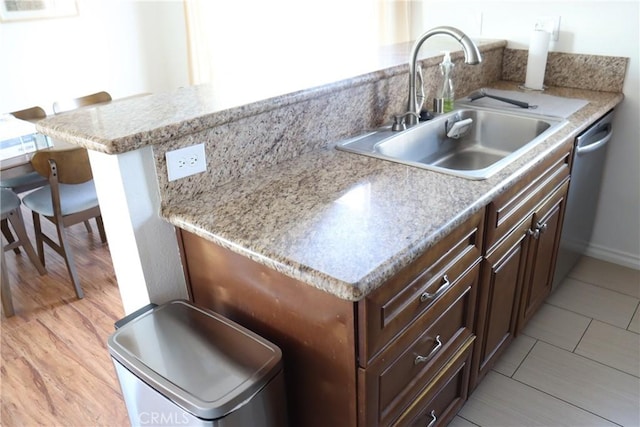 kitchen featuring dark brown cabinetry, a breakfast bar area, a peninsula, a sink, and stainless steel dishwasher