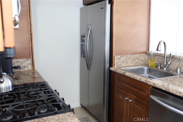 kitchen with appliances with stainless steel finishes, a sink, and light stone counters