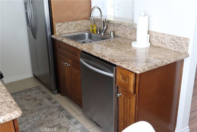 kitchen featuring brown cabinetry, appliances with stainless steel finishes, light stone counters, a sink, and light tile patterned flooring