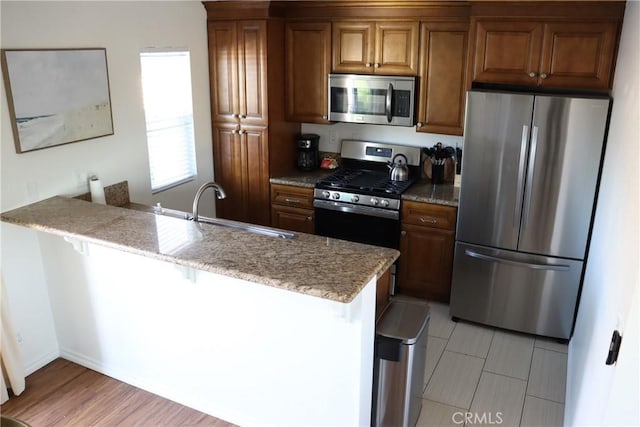 kitchen featuring brown cabinets, a breakfast bar area, stainless steel appliances, a sink, and light stone countertops