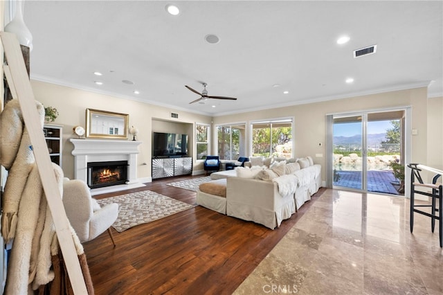 living room featuring crown molding, recessed lighting, visible vents, a glass covered fireplace, and wood finished floors