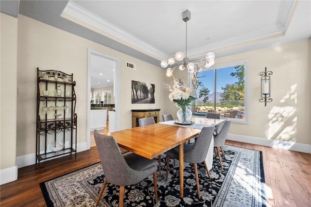 dining space featuring crown molding, dark wood-type flooring, a raised ceiling, and an inviting chandelier