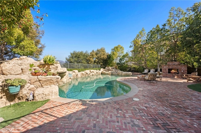 view of pool featuring fence, an outdoor stone fireplace, a fenced in pool, and a patio