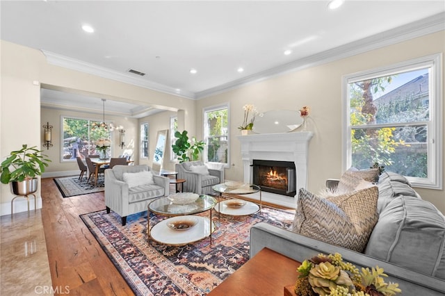 living area with a warm lit fireplace, baseboards, visible vents, crown molding, and light wood-style floors