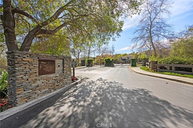 view of road featuring a gate, curbs, sidewalks, and a gated entry