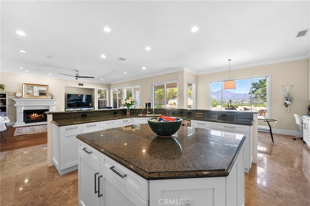 kitchen with crown molding, open floor plan, a sink, a warm lit fireplace, and a large island with sink