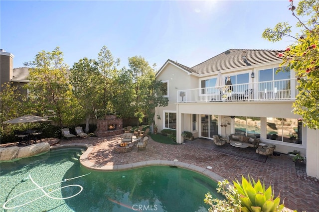 back of property with a tile roof, a patio area, a balcony, an outdoor pool, and a lit fireplace