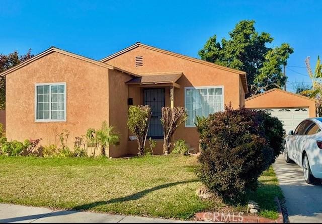 view of front of house featuring a detached garage, a front lawn, and stucco siding