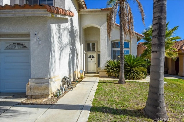 entrance to property featuring a yard, an attached garage, and stucco siding