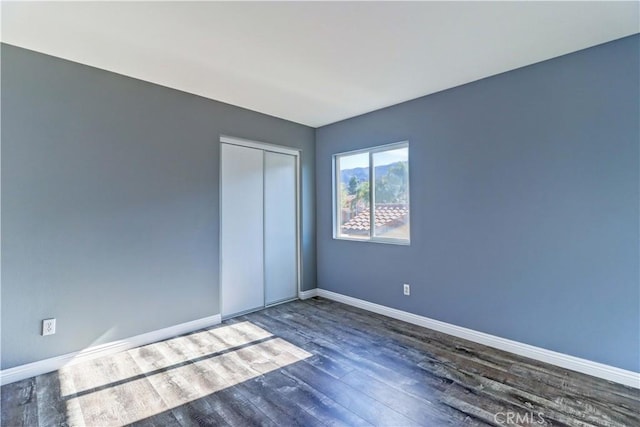 unfurnished bedroom with a closet, dark wood finished floors, and baseboards