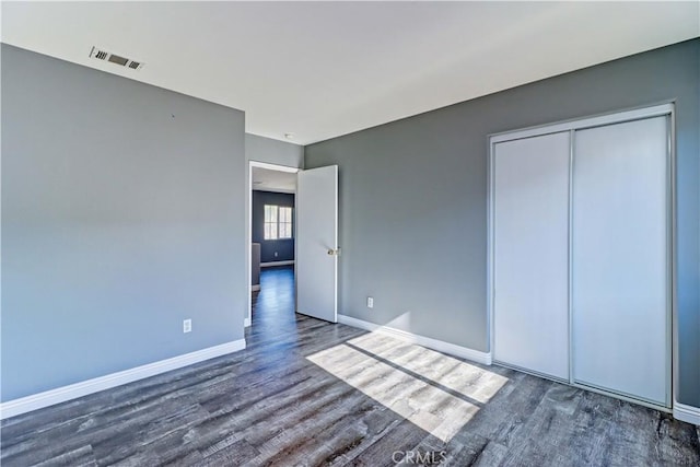 unfurnished bedroom featuring a closet, visible vents, baseboards, and wood finished floors