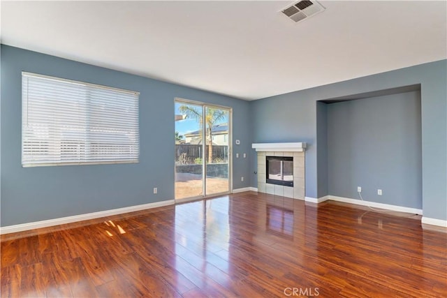 unfurnished living room with wood finished floors, a tile fireplace, visible vents, and baseboards