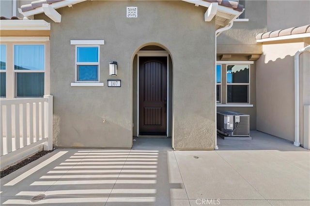 view of exterior entry featuring central air condition unit, a tiled roof, and stucco siding