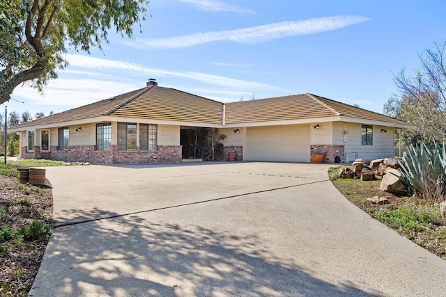 ranch-style home featuring a garage, a chimney, concrete driveway, and brick siding