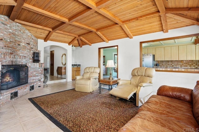 living area with vaulted ceiling with beams, light tile patterned floors, wooden ceiling, visible vents, and a brick fireplace