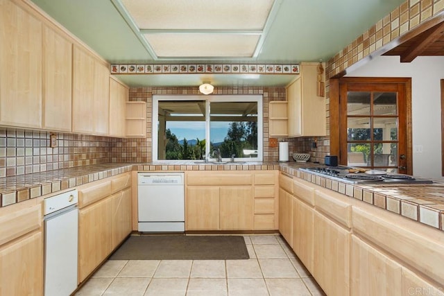 kitchen with open shelves, white dishwasher, tile countertops, and light brown cabinetry