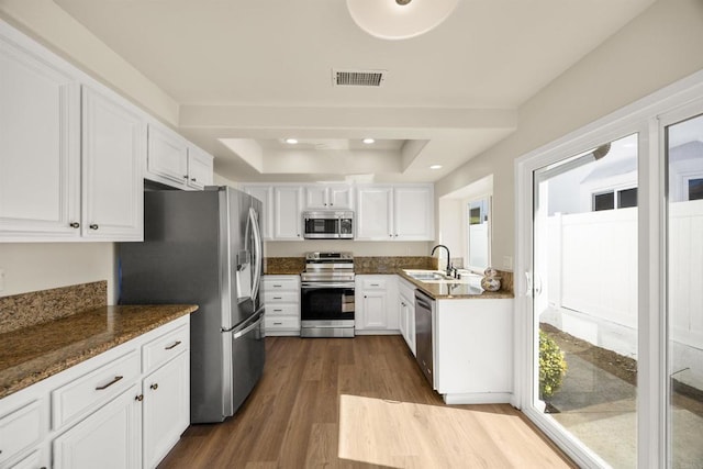 kitchen featuring visible vents, dark stone countertops, stainless steel appliances, white cabinetry, and a sink