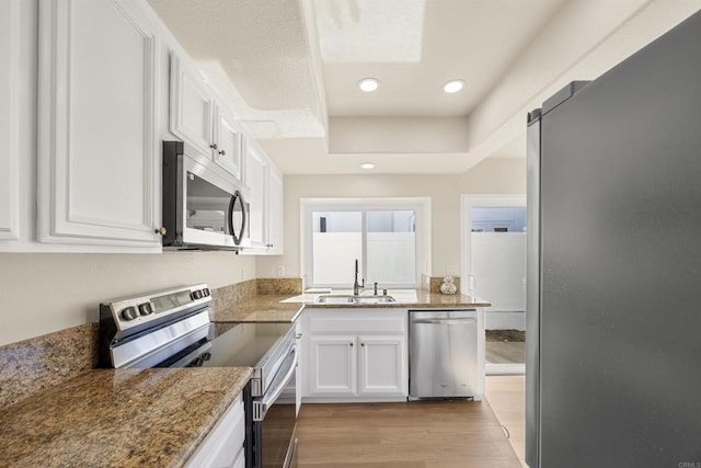 kitchen featuring stainless steel appliances, light wood-type flooring, stone counters, white cabinetry, and a sink